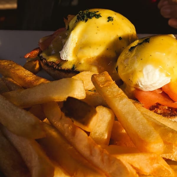 Open-faced breakfast sandwich topped with poached eggs and tomatoes, served with golden fries on a plate.