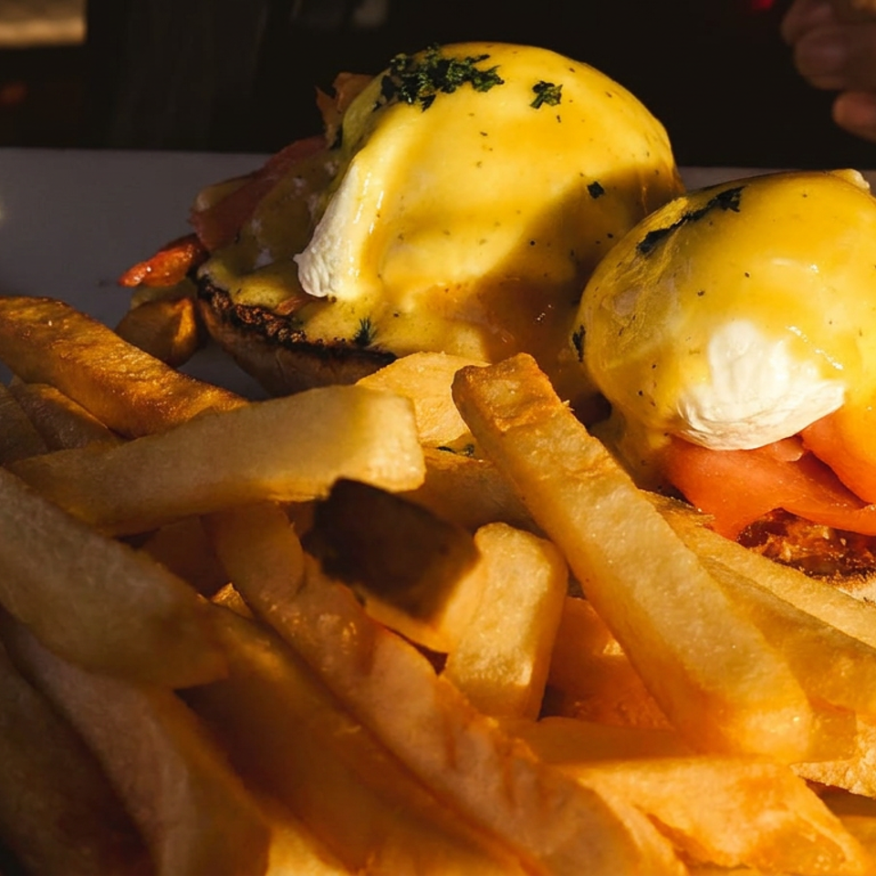 Open-faced breakfast sandwich topped with poached eggs and tomatoes, served with golden fries on a plate.