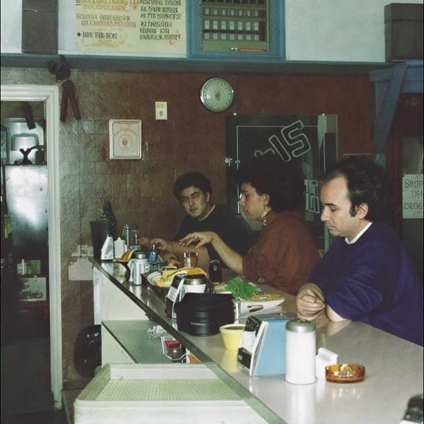 Three diners sit at a counter in Rocky’s Breakfast restaurant, with menus, condiments, and breakfast plates visible.