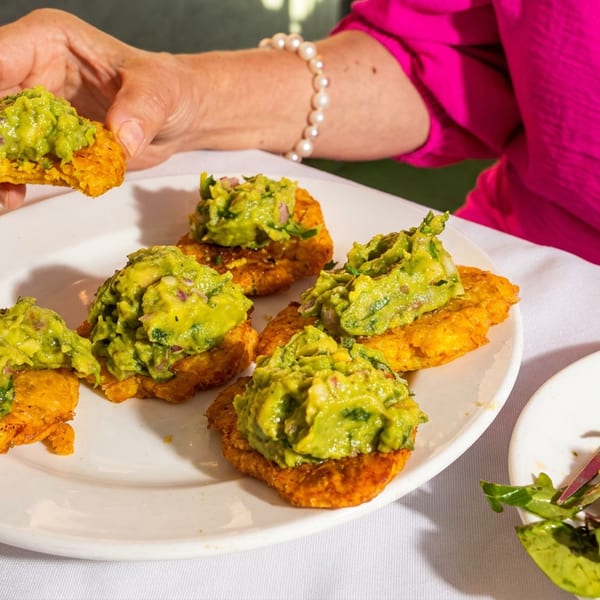 Golden corn cakes topped with chunky guacamole on a plate, with a side salad and diner lifting one cake.