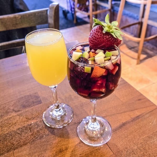 Bright orange drink and fruit-filled sangria garnished with a large strawberry, served on a wooden restaurant table.